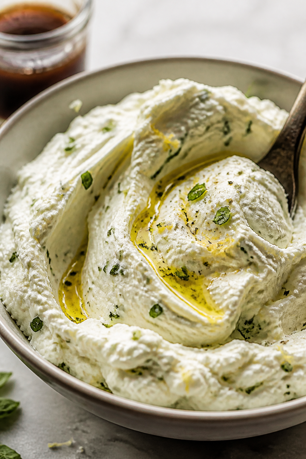 Close-up detail of the herbed ricotta being whipped to a silky, cloud-like texture in a shallow bowl