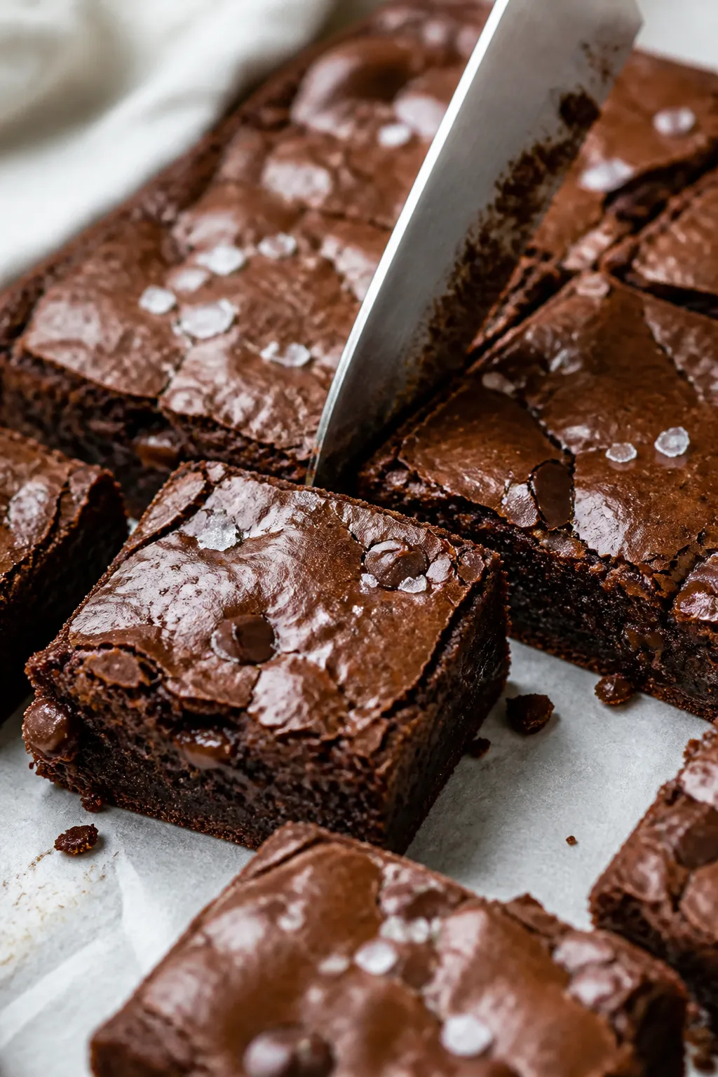 Close-up detail: Freshly baked chocolate fudge squares being sliced on parchment after cooling, capt
