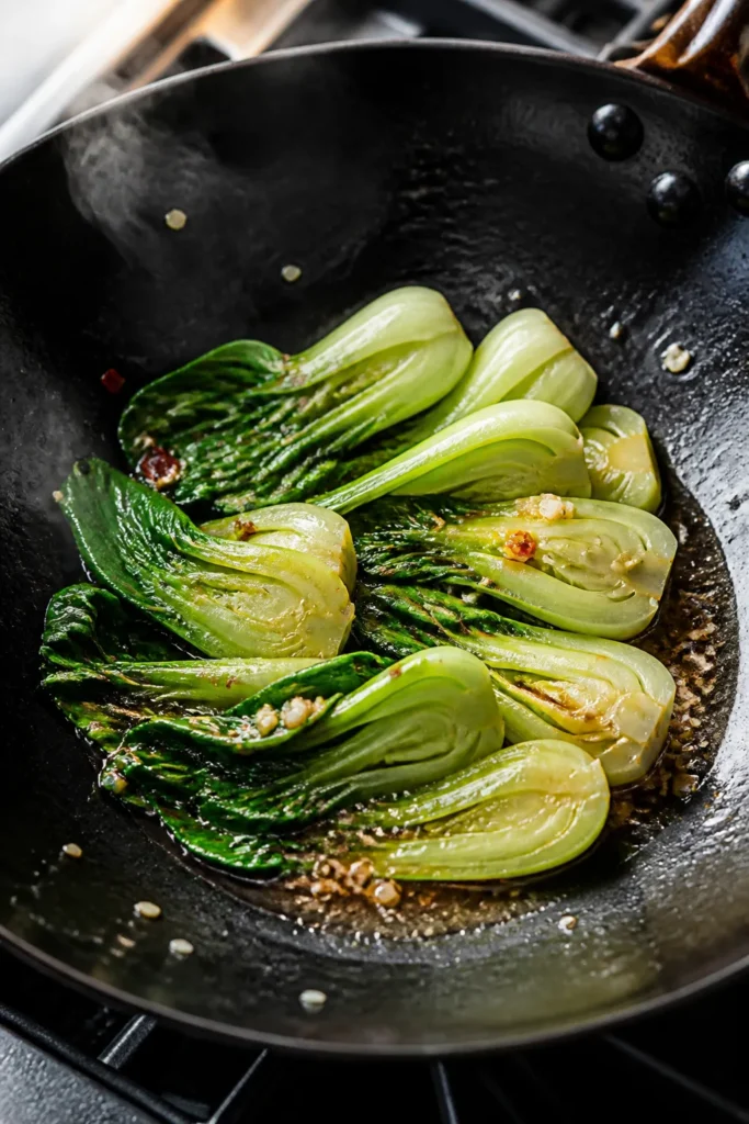 Cooking process close-up: Baby bok choy halves sizzling in a carbon-steel wok over medium-high heat,